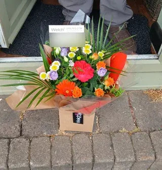 Orange roses and mixed flowers in a Welch carrier