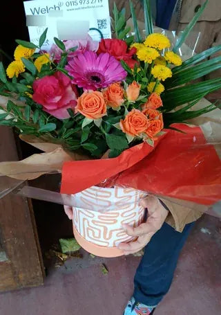 Pink gerbera and orange roses in a patterned container