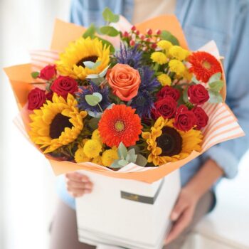 Vibrant bouquet with sunflowers, roses, and gerbera daisies in a white box. The Sunflower Celebration, an Autumn Bouquet from Welch the Florist | Next Day Flower Delivery UK Florist.