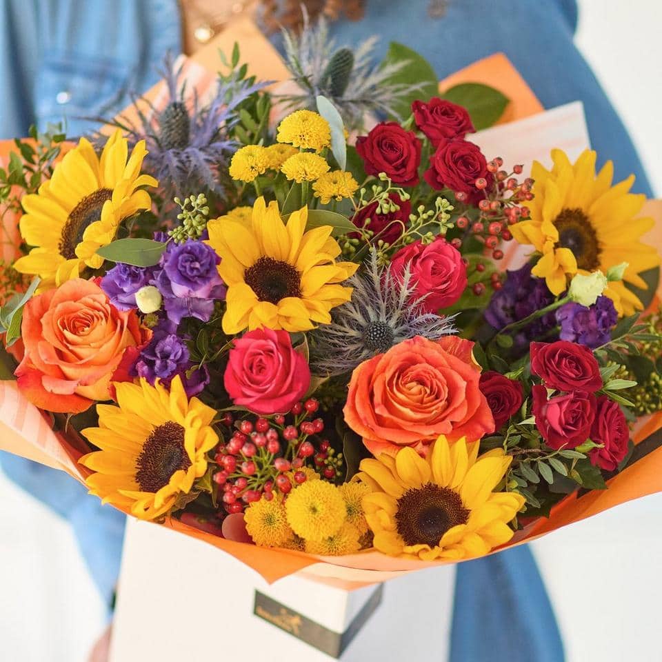 Bright sunflower, red roses, and purple flowers in a colourful bouquet for celebrations. The Sunflower Carnival, an Autumn Bouquet from Welch the Florist | Next Day Flower Delivery UK Florist.